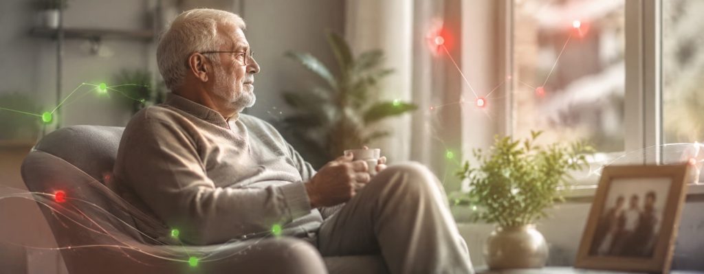 Älterer Mann sitzt mit einer Tasse im Sessel am Fenster seiner Wohnung